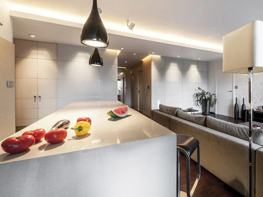 A curved pale kitchen island beneath black pendants, with tomatoes on the benchtop.