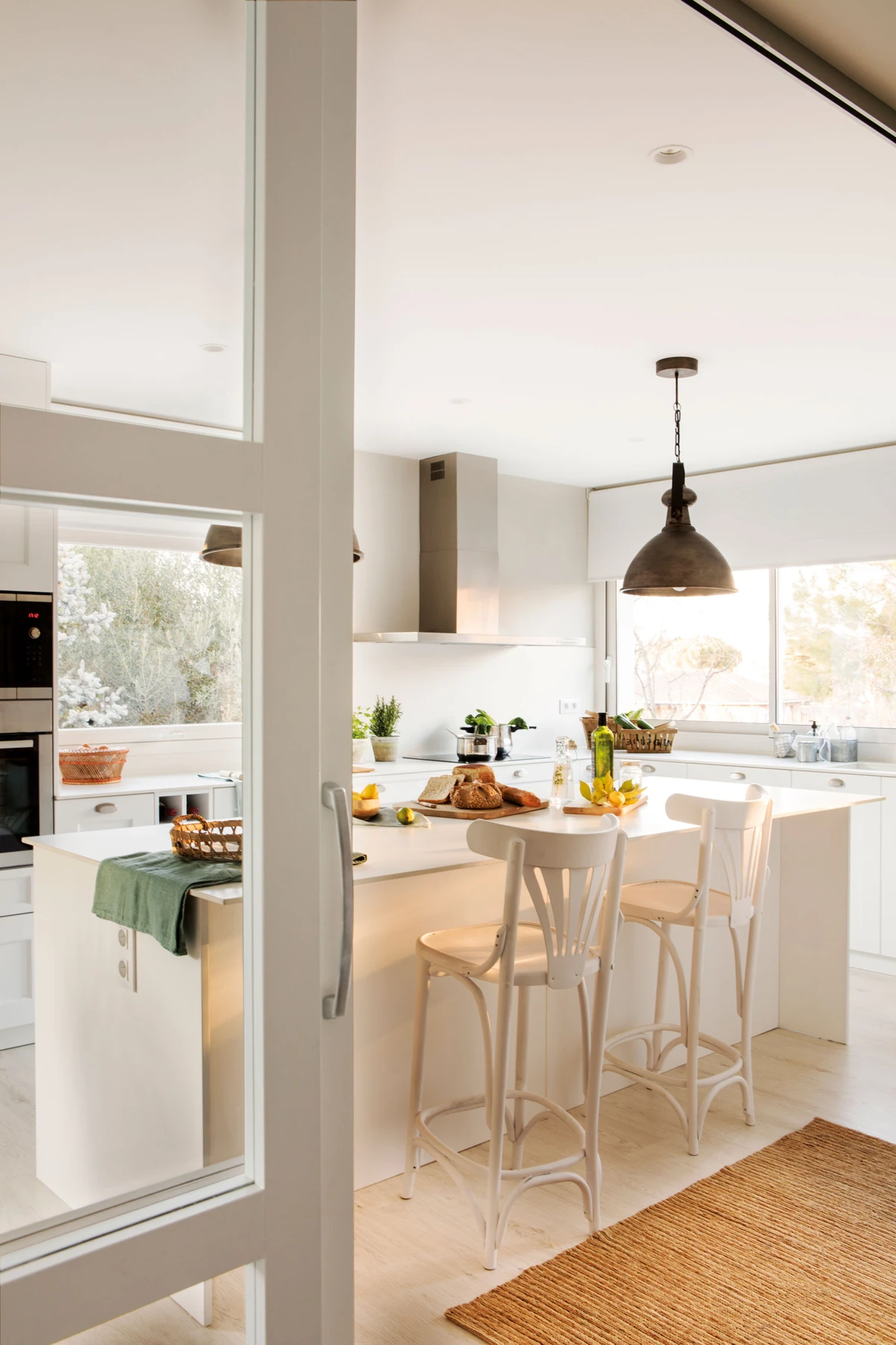 A bright kitchen seen through an open doorway, with a light island and timber stools.
