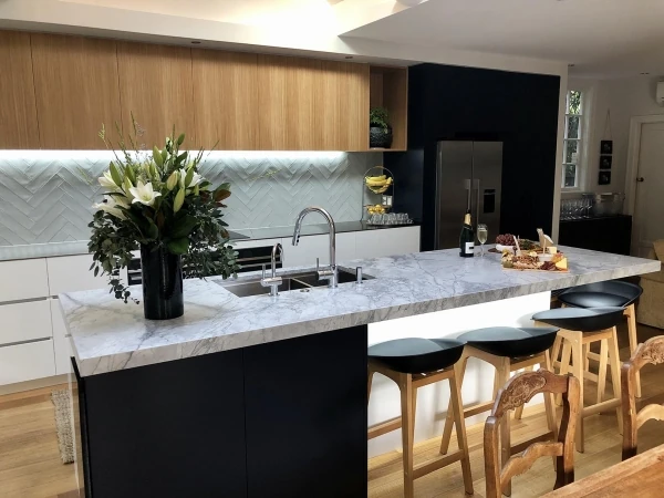 Light veined island with dark cabinetry, timber cupboards and woven bar stools.