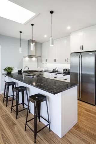 White kitchen with a dark island, bar stools and a skylight above the timber floor.