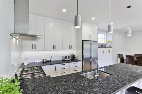 White kitchen with a dark speckled island, inset sink and pendant lighting.