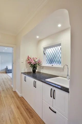 Kitchen sink beneath a bright window, with a dark benchtop and white cupboards.
