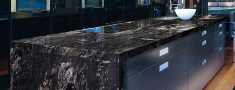 Dark waterfall benchtop with bold pale veining and black cabinetry.