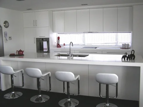 Light kitchen island with curved white bar stools beside a large window.