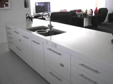 White kitchen island with a double sink and open-plan seating beyond.