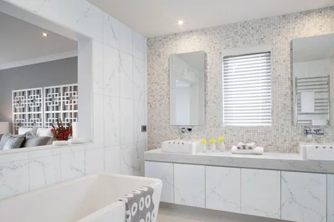 Bathroom with a double vanity, freestanding bath and pale veined surfaces.