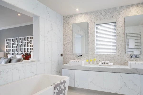 Bathroom with a double vanity, freestanding bath and pale veined surfaces.