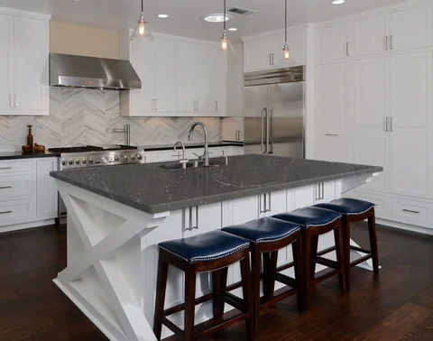 Grey benchtop on a white kitchen island with blue upholstered stools.