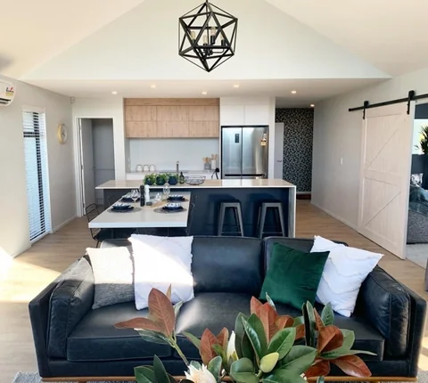 Open-plan living room beside a dark kitchen island and timber cabinetry.