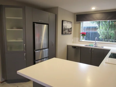 Light kitchen peninsula beside grey cabinetry and a wide window.