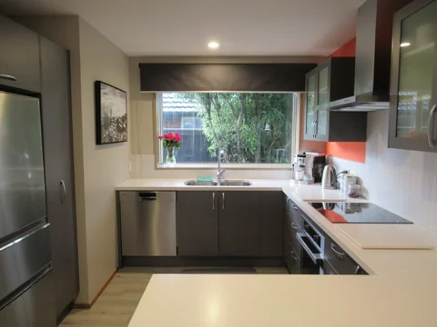 Light benchtop and kitchen sink beneath a window, with dark lower cupboards.