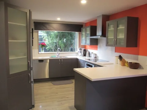 Light kitchen peninsula with grey cabinetry, a red wall and a stainless steel rangehood.