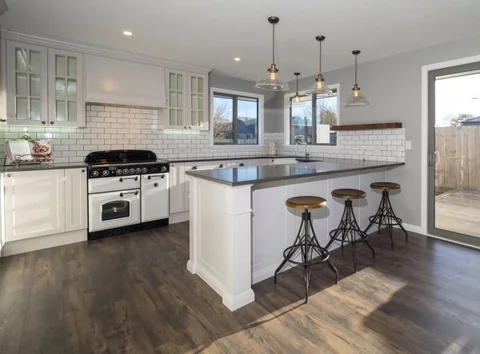 White island with a dark benchtop, bar stools and pendant lighting.