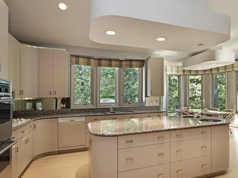 Curved island and cream cabinetry beside large corner windows.