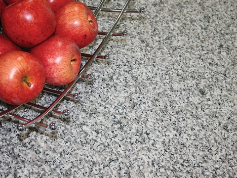 Close view of a speckled benchtop with a basket of red apples.