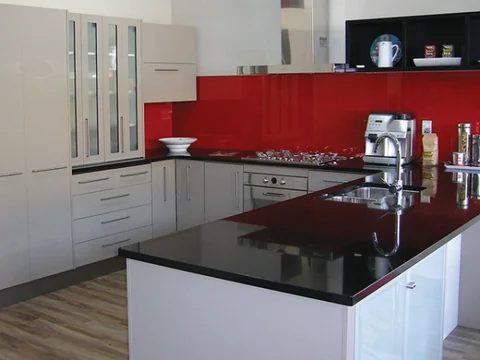 Glossy dark benchtop with a white sink, red splashback and white cupboards.