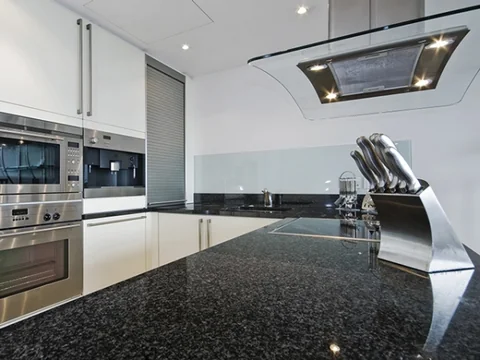 Curved white kitchen with a dark benchtop, inset sink and stacked ovens.