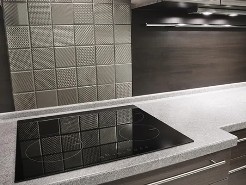 Light grey benchtop with a black cooktop and a square metal splashback.