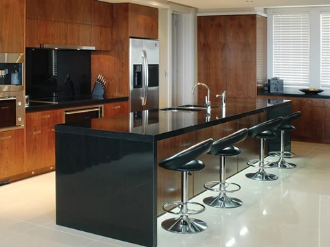 Long dark kitchen island with timber cabinetry and black bar stools.