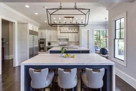 Classic white kitchen with a large light island and white chairs.