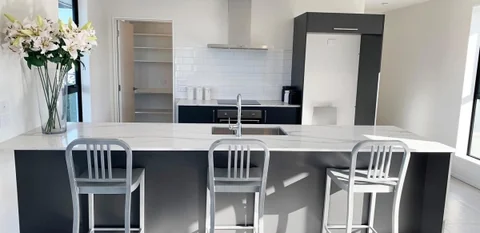 Wide view of a light benchtop on a dark island with white stools.