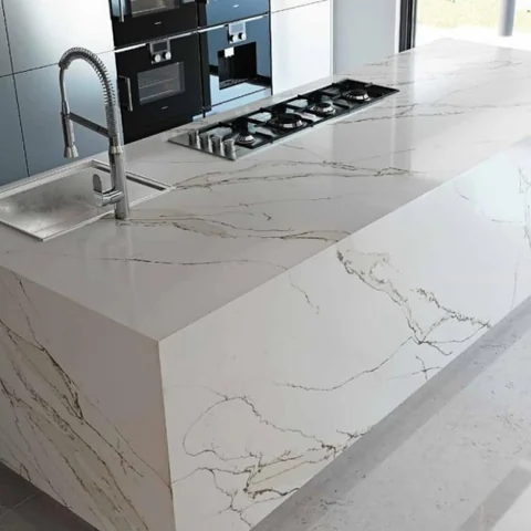 Pale veined waterfall island with a gas cooktop and dark flooring.