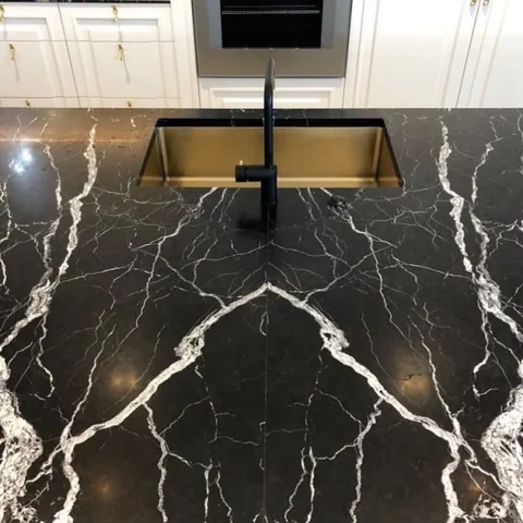 Dark veined bathroom bench with a gold-coloured basin and black tap.