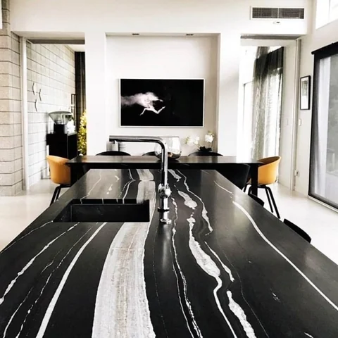Long dark island with bold veining and black kitchen cabinetry.