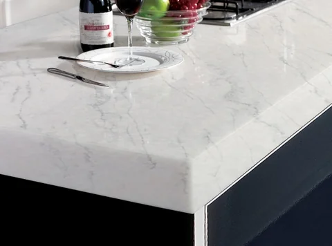 Detail of a pale veined waterfall benchtop beside a bottle and glass.