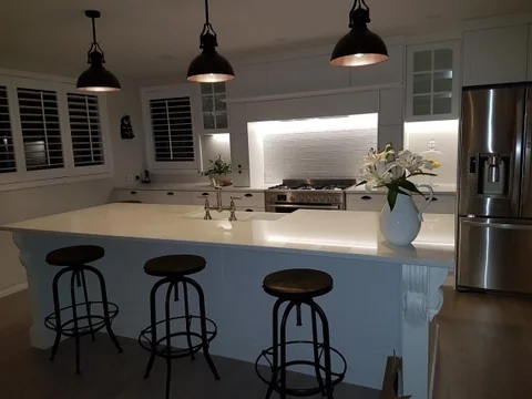 Grey-blue kitchen island with a pale benchtop, bar stools and black pendants.