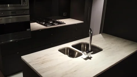 Dark kitchen with a pale benchtop, double sink and built-in cooktop.