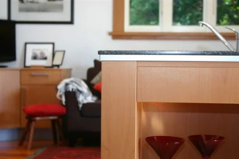 Timber kitchen benchtop with red stools beside a window.