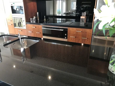 Dark kitchen benchtop and inset sink with timber cabinetry.